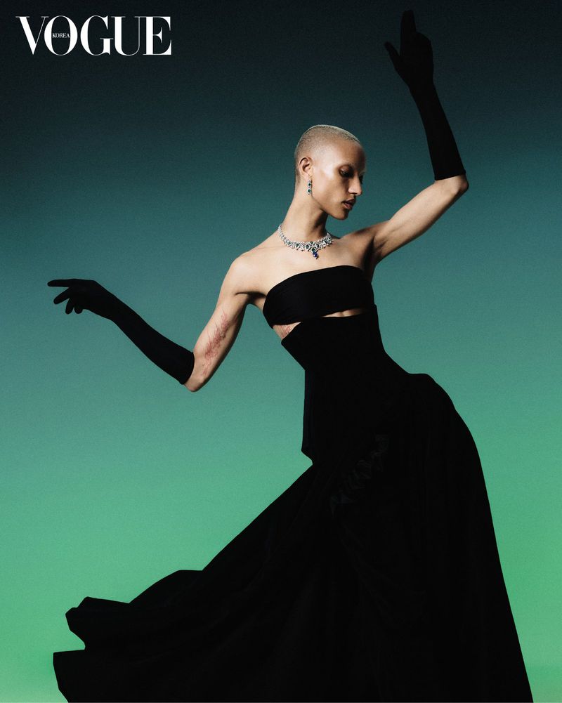 Fashion editorial image of a woman in a black dress and gloves posing against a gradient turquoise background for Vogue Korea magazine.