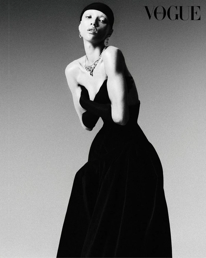 Model Georgia Palmer wearing a black strapless gown, opera gloves, and diamond necklace against a grey backdrop.