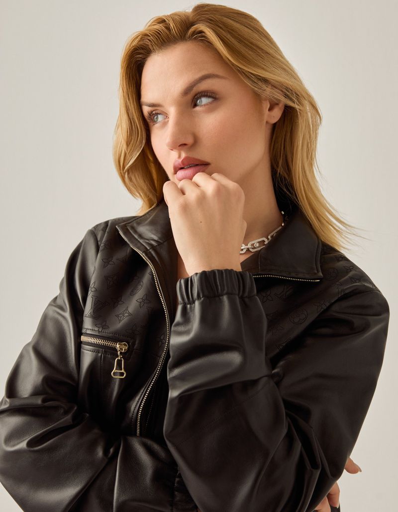 Blonde woman in a black jacket looking away with her hand near her face in a studio environment, illuminated by soft lighting.