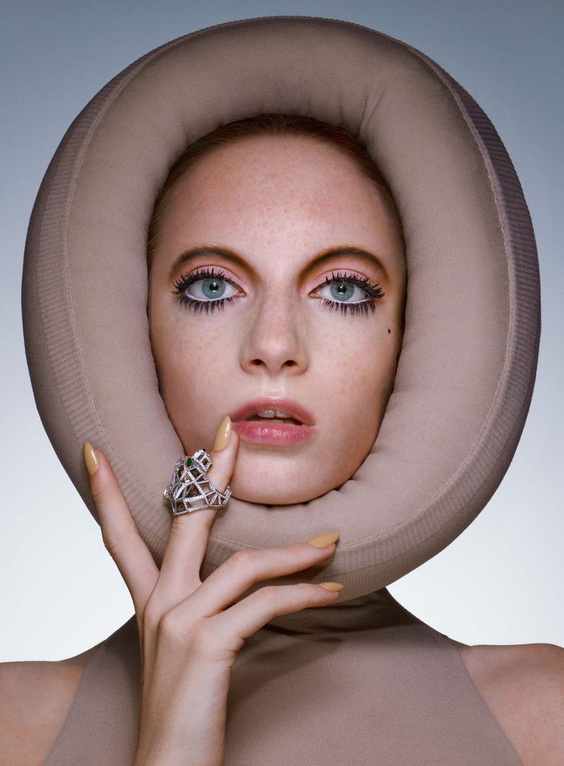 Close-up portrait of a young fair-skinned adult female model with blue eyes wearing a beige head covering and statement jewelry ring.
