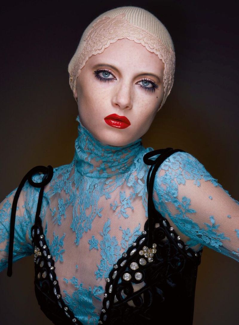 Portrait of a person wearing a blue lace top and a black dress with jewels, posing against a dark backdrop in a studio setting.