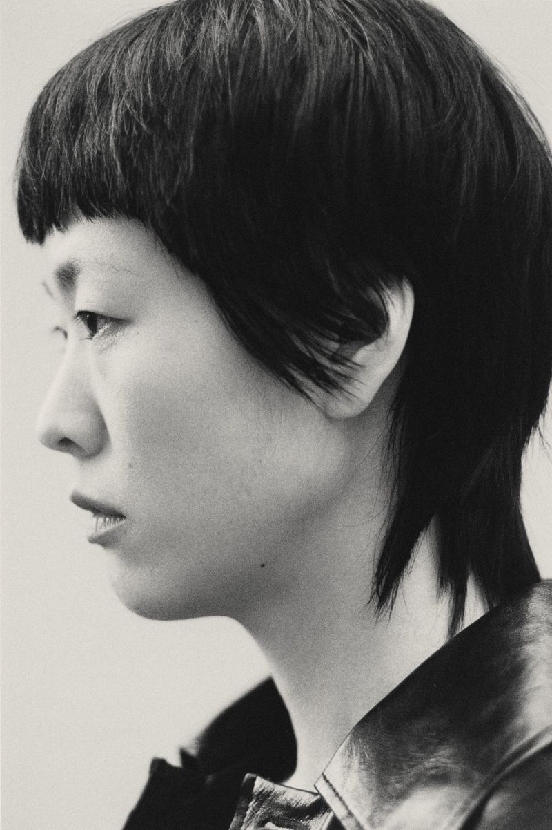 Monochromatic portrait of an Asian woman with short hair in profile, wearing a black leather jacket against a plain background.