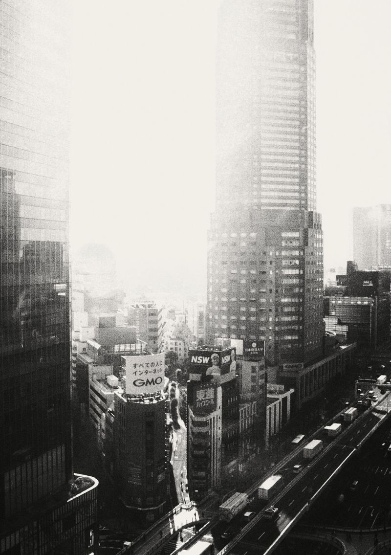 High-angle black and white shot of Tokyo cityscape with skyscrapers, busy streets, and signage on buildings during daytime.