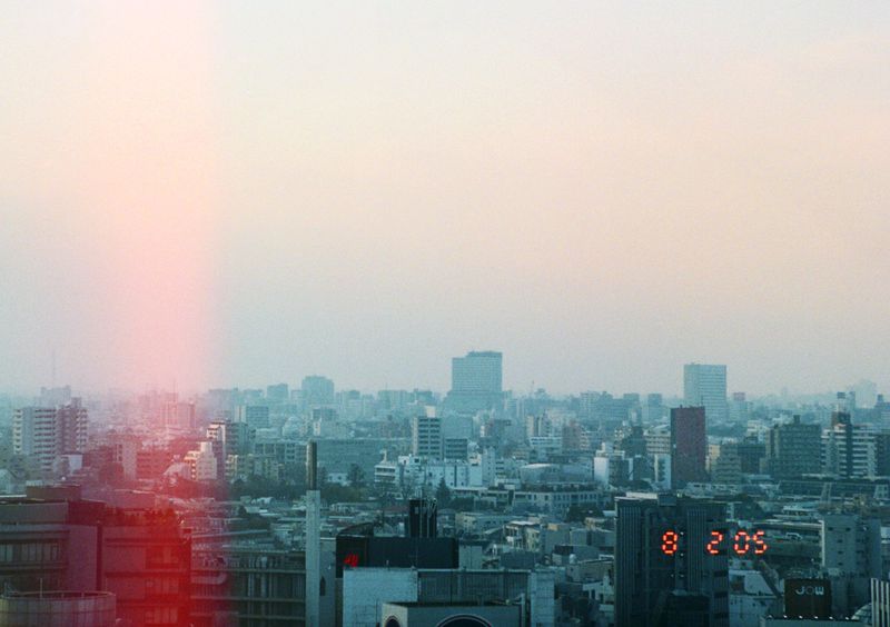 Cityscape view of dense urban buildings under a hazy sky at dawn or dusk, with an illuminated digital clock tower.