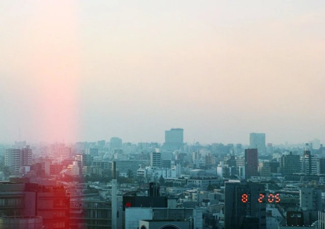 Cityscape view of dense urban buildings under a hazy sky at dawn or dusk, with an illuminated digital clock tower.