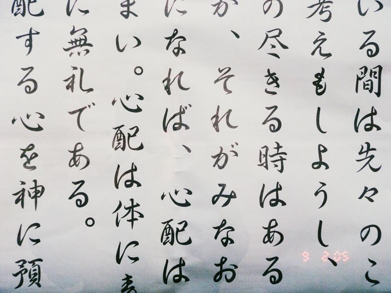 Calligraphy of Japanese script in black ink on white paper, featuring vertical lines of text with a digital clock display at bottom.
