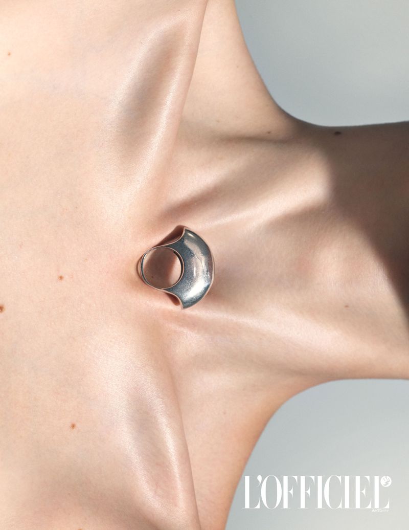 Silver abstract earring on woman's ear against a grey background, highlighting modern jewelry design and clean aesthetic.