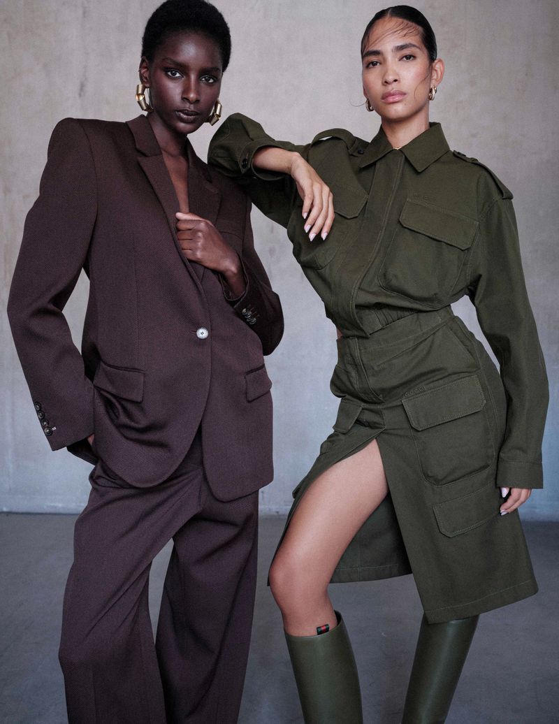 Two adult women pose in fashionable tailored clothing against a neutral background in a studio portrait. Fashion and style editorial.