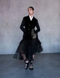 Model wearing a black velvet jacket and layered tulle skirt against a textured grey wall for L Officiel Italia.