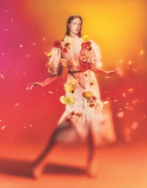 Model in a white dress adorned with colorful fresh flowers against a warm red and yellow gradient background