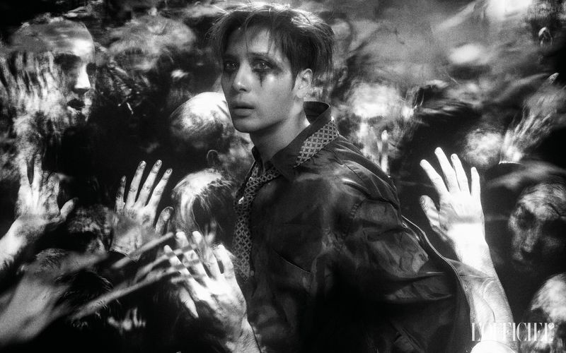 Dramatic black and white portrait of a stylish male surrounded by blurred figures, moody lighting, and wearing a button-down shirt with tie.