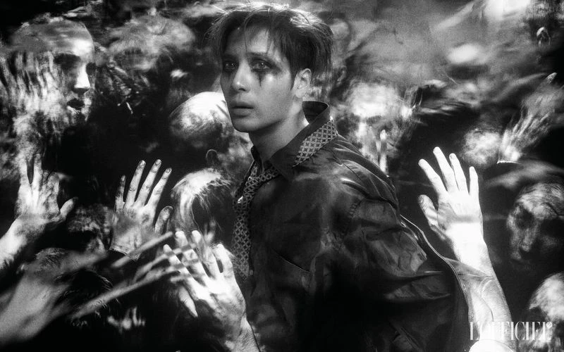 Dramatic black and white portrait of a stylish male surrounded by blurred figures, moody lighting, and wearing a button-down shirt with tie.