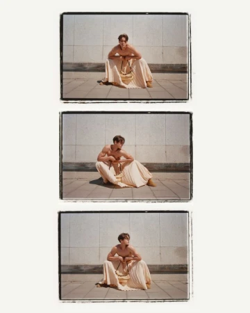 Three film-strip style frames show a shirtless male model sitting outside, wearing a tan skirt and beaded necklace, posing against a wall.