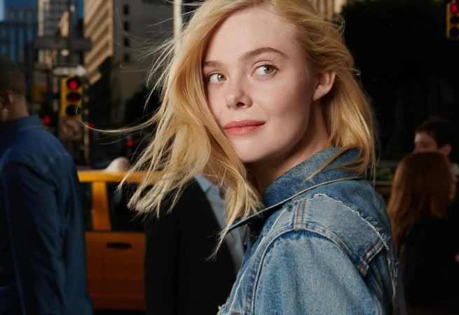 Close-up of a blonde woman in a denim jacket in a city, featuring a blurred yellow taxi and pedestrians in the background.