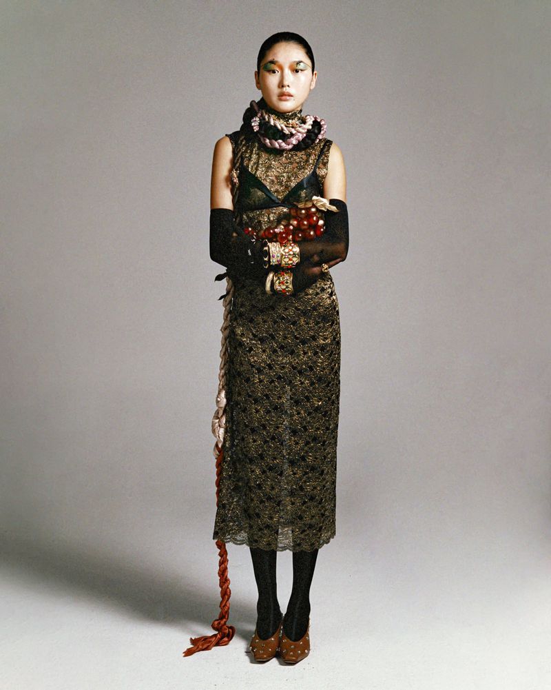 A full studio shot of an Asian woman wearing a patterned dress and unique jewelry, holding what appears to be cranberries.