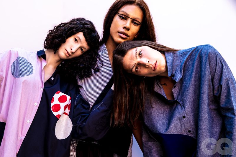 Three people wearing color-blocked shirts pose together against a white background in a fashion shot. The image has GQ branding.