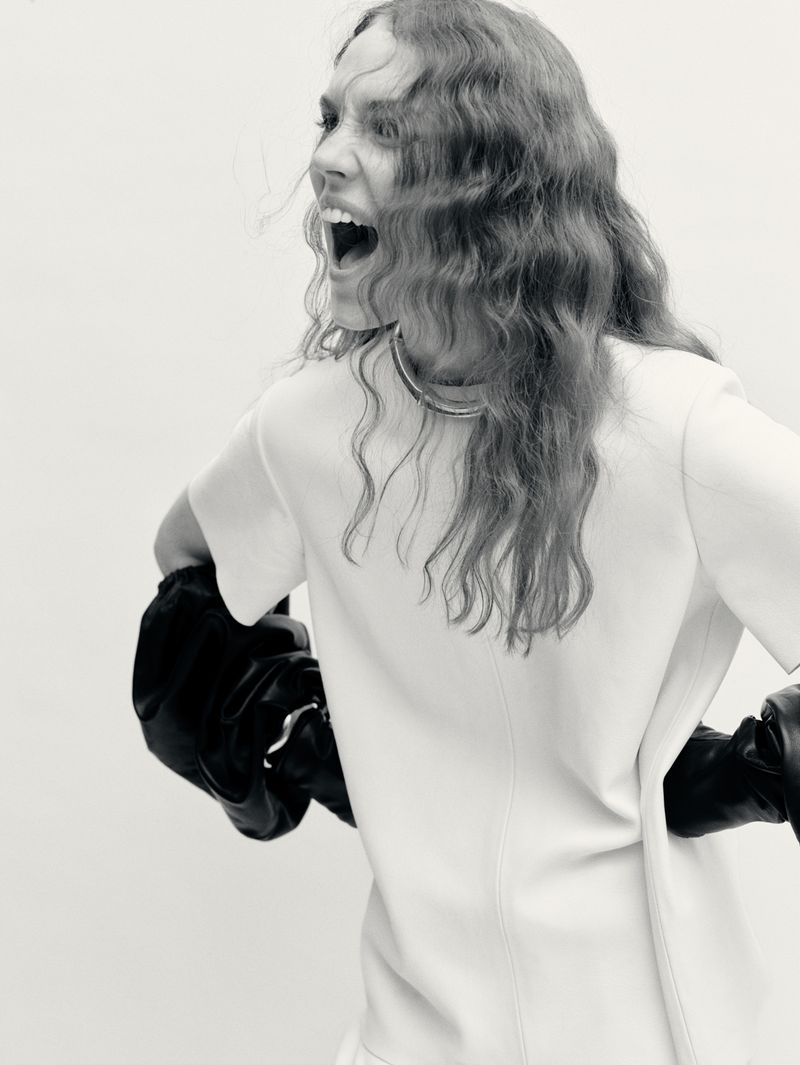 Woman in short-sleeved dress and boxing gloves turns away from camera, yelling. Black and white studio shot with bright lighting.