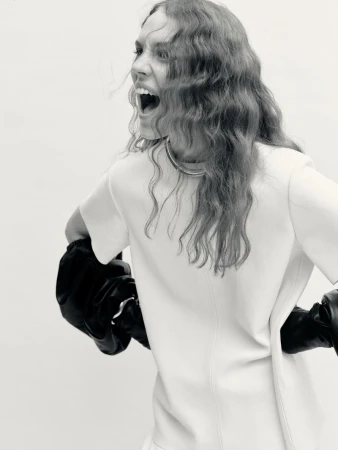 Woman in short-sleeved dress and boxing gloves turns away from camera, yelling. Black and white studio shot with bright lighting.