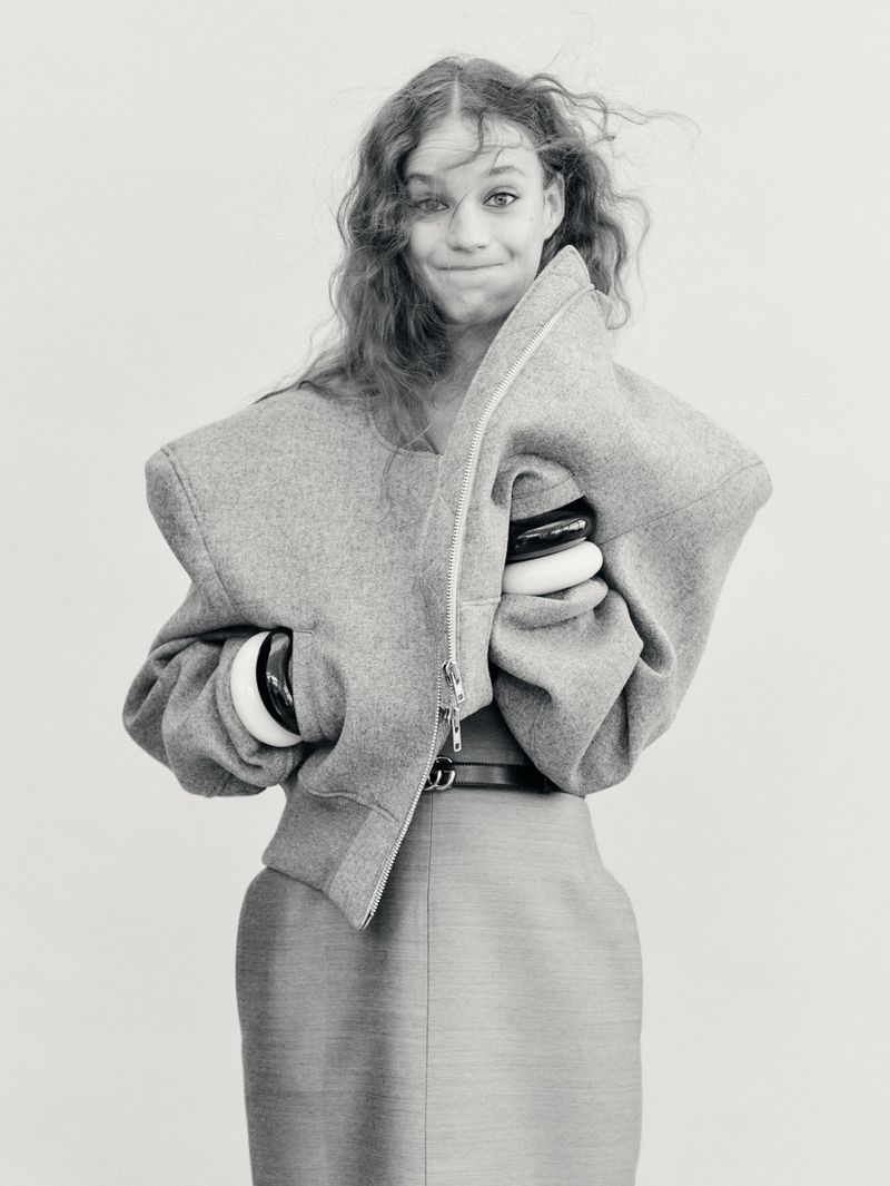 Monochromatic portrait of a young woman with curly hair holding a gray jacket and accessorized with black and white bracelets.