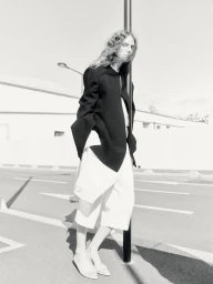 Model Gwen Weijers leaning against a pole on a paved street wearing a black jacket and white shorts in a black and white editorial image.