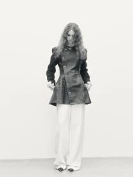 Model Gwen Weijers wearing a dark asymmetric coat and light trousers against a neutral background.