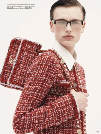 Fashion editorial shot of a stylish woman wearing a tweed Chanel suit, carrying a matching handbag, and wearing eyeglasses against a white backdrop.