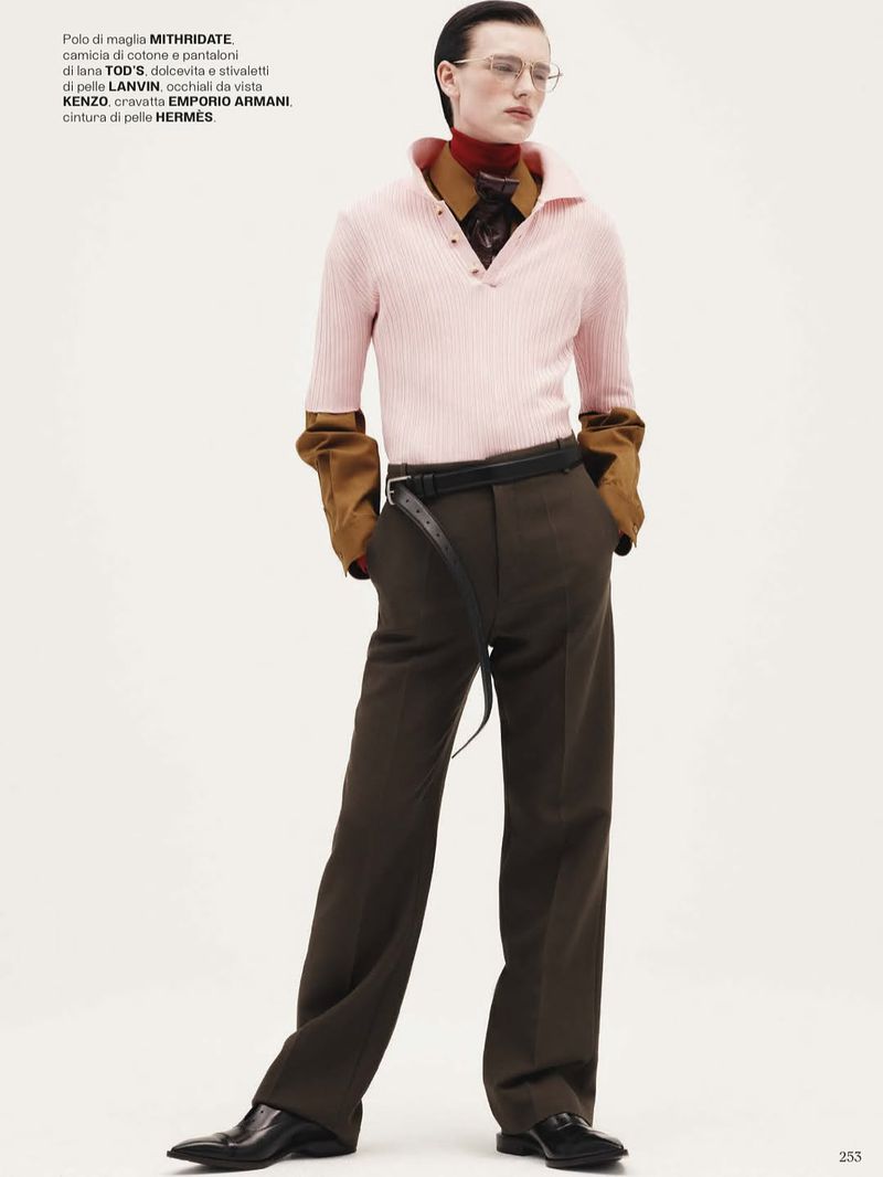 Editorial fashion shot: adult male model in studio wearing a pink top, brown trousers, glasses, and black leather shoes. 