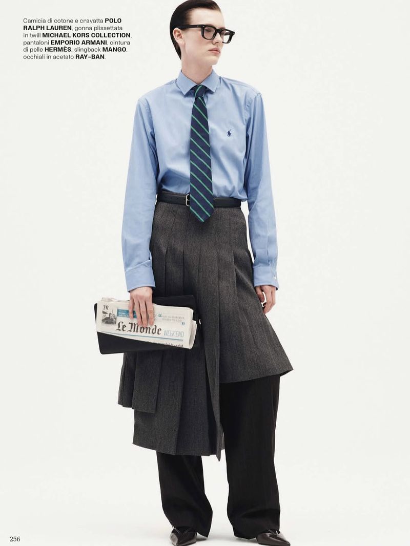 Editorial fashion shot of a young adult male with black hair wearing glasses, a light blue shirt, tie, grey skirt, and carrying newspaper.