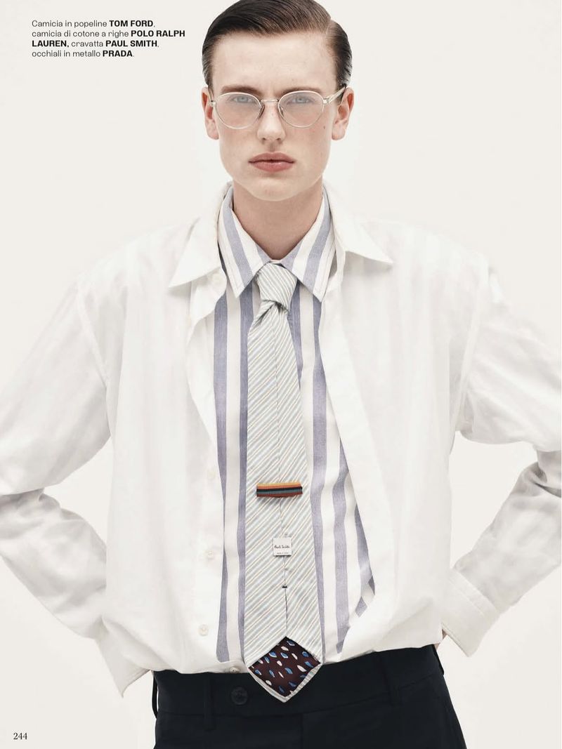 Man in white shirt, striped shirt, and tie. He wears glasses and has his hands on his hips against a clean, light background.