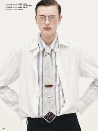 Man in white shirt, striped shirt, and tie. He wears glasses and has his hands on his hips against a clean, light background.