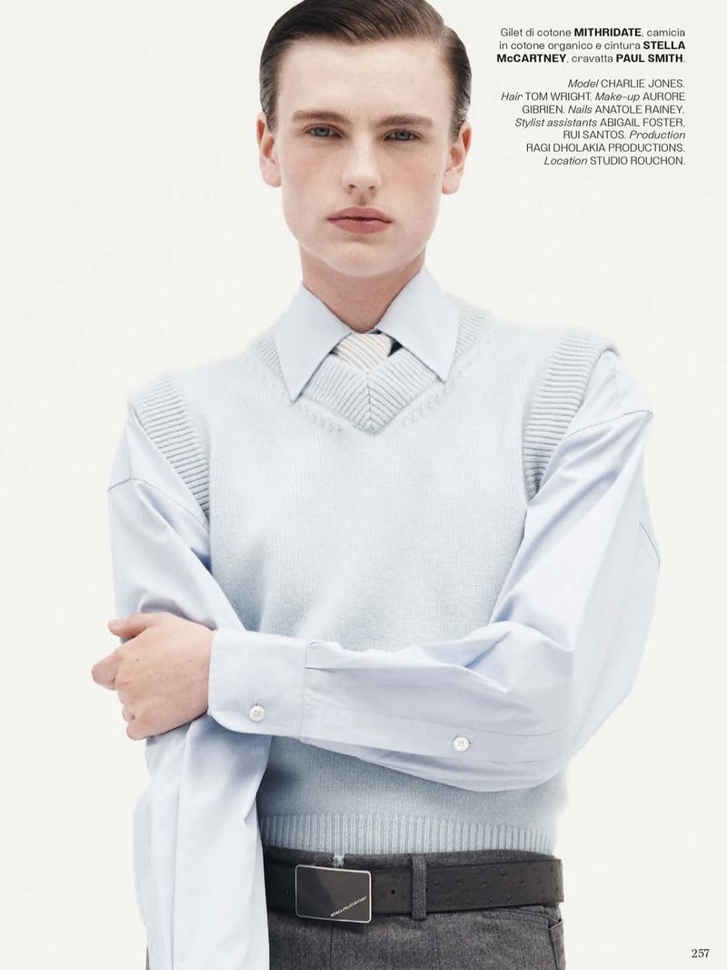 Portrait of a light-skinned male model wearing a light blue shirt and sweater vest, looking directly at the camera in a photo studio.