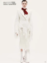 Model in white fringed tweed jacket with red bow tie standing against plain white backdrop