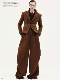 Model in a brown tailored suit with glasses posing against a white seamless background for Vogue Italia.
