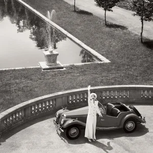 Model Jeanne Cadieu waving beside a vintage car near a pool for Vogue France by Steven Meisel