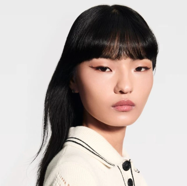 Close-up studio shot of a young Asian woman with black hair and subtle makeup, wearing a white top against a clean white background.