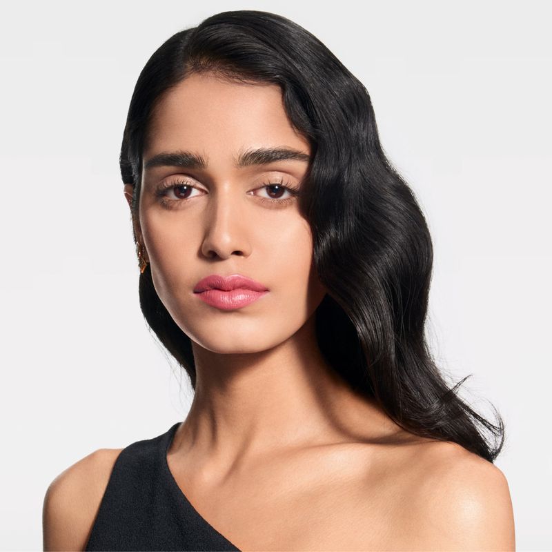 Close-up portrait of an adult woman with dark wavy hair and pink lipstick, set against a clean white background in a beauty context.