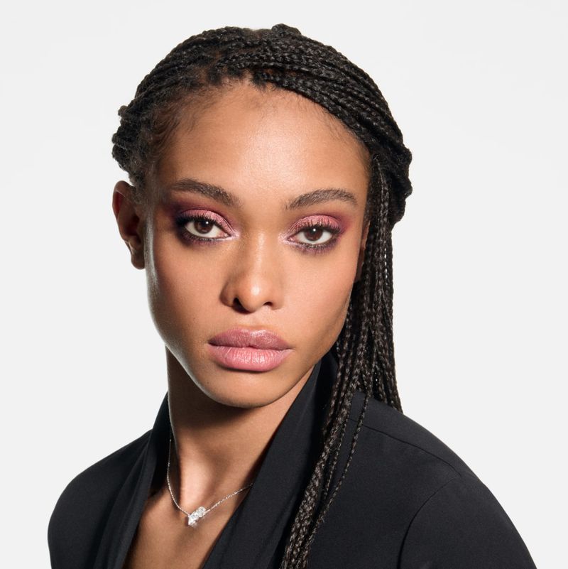 Close-up studio shot of an adult female with braided hair, wearing a silver necklace and black jacket against a white backdrop.