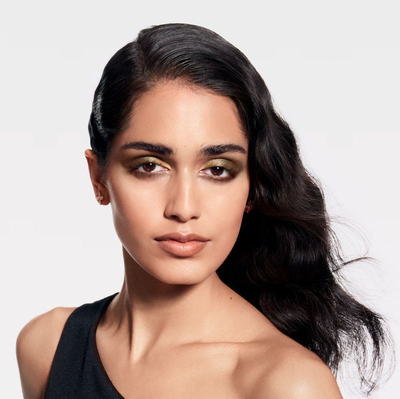 Model Ashley Radjarame posing in a black one-shoulder top with metallic eyeshadow against a clean white seamless studio background.