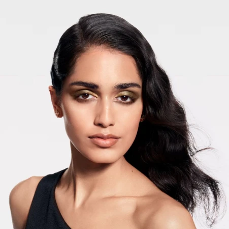 Model Ashley Radjarame posing in a black one-shoulder top with metallic eyeshadow against a clean white seamless studio background.