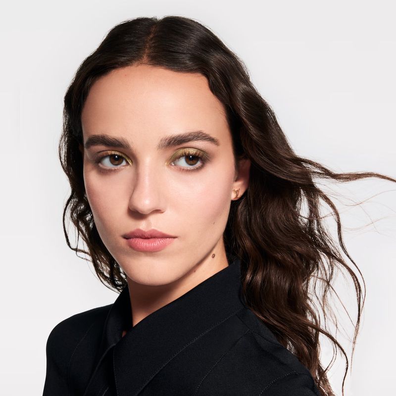 Close-up beauty portrait of a young adult woman with brunette hair and olive eyeshadow wearing a black button-down shirt against white.