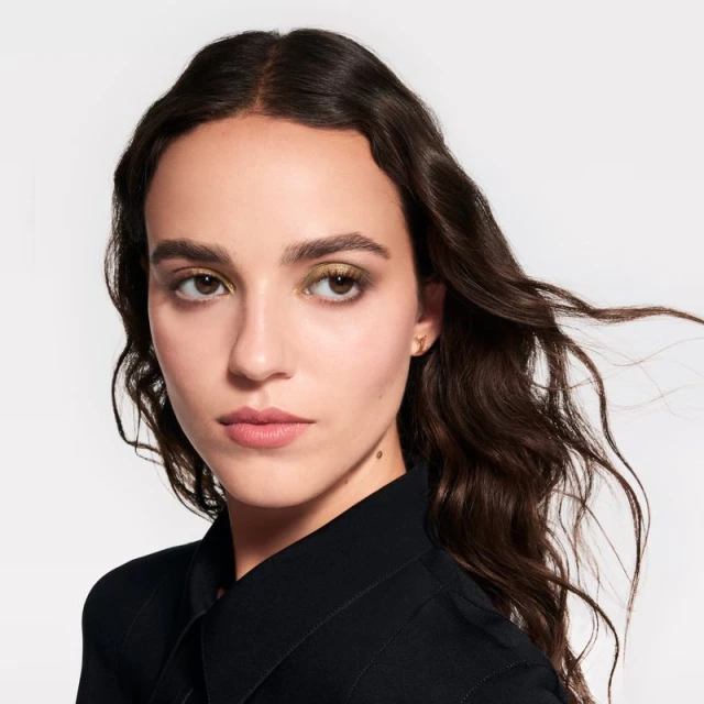 Close-up beauty portrait of a young adult woman with brunette hair and olive eyeshadow wearing a black button-down shirt against white.