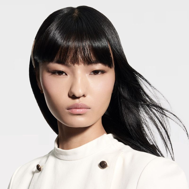 Headshot of an Asian woman with black hair and fair skin, posing in a white top against a neutral background, creating a minimalist fashion portrait.