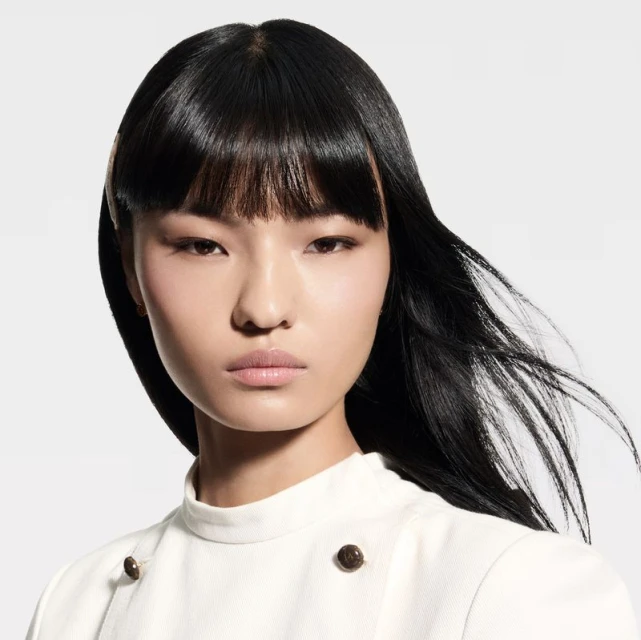 Headshot of an Asian woman with black hair and fair skin, posing in a white top against a neutral background, creating a minimalist fashion portrait.