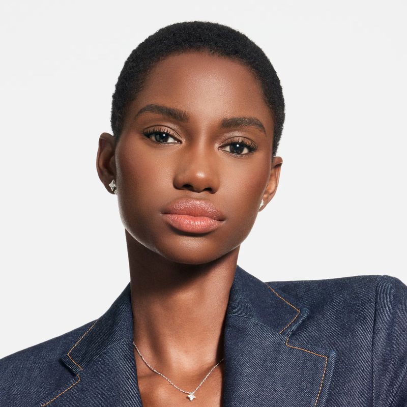 Close-up of a young Black woman with short hair, wearing a denim jacket and jewelry, posing against a white background in a studio setting.