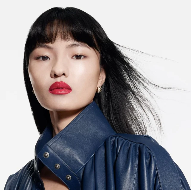 Glamorous portrait of an Asian woman with black hair, vibrant red lipstick, wearing a navy leather jacket against a white backdrop.
