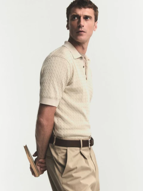 Portrait of an adult male in a polo shirt and khaki pants, holding a book in front of a white backdrop, looking off-camera with a serious expression.