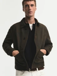 Model Clement Chabernaud wearing dark brown jacket and white trousers against white background