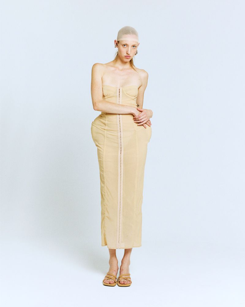 Woman in a beige strapless dress and sandals, standing against a white backdrop in a fashion-style full studio shot.