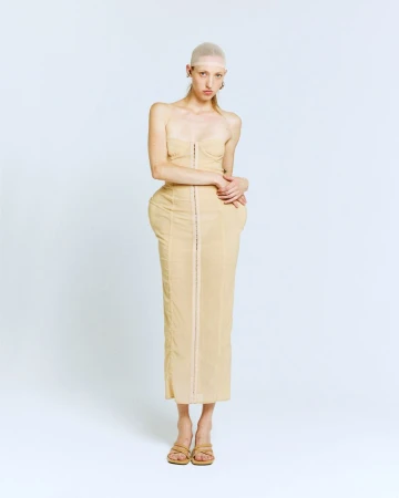 Woman in a beige strapless dress and sandals, standing against a white backdrop in a fashion-style full studio shot.