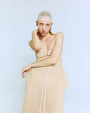 Model wearing a structured beige strapless dress and nude hair cap posing against a pale background for Georgiela Studio